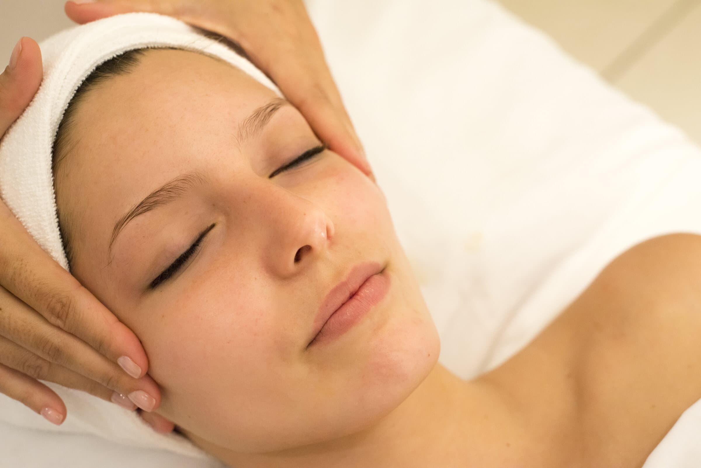 Entspannte Frau mit Stirnband bei einer Gesichtsmassage, zwei Hände an den Schläfen